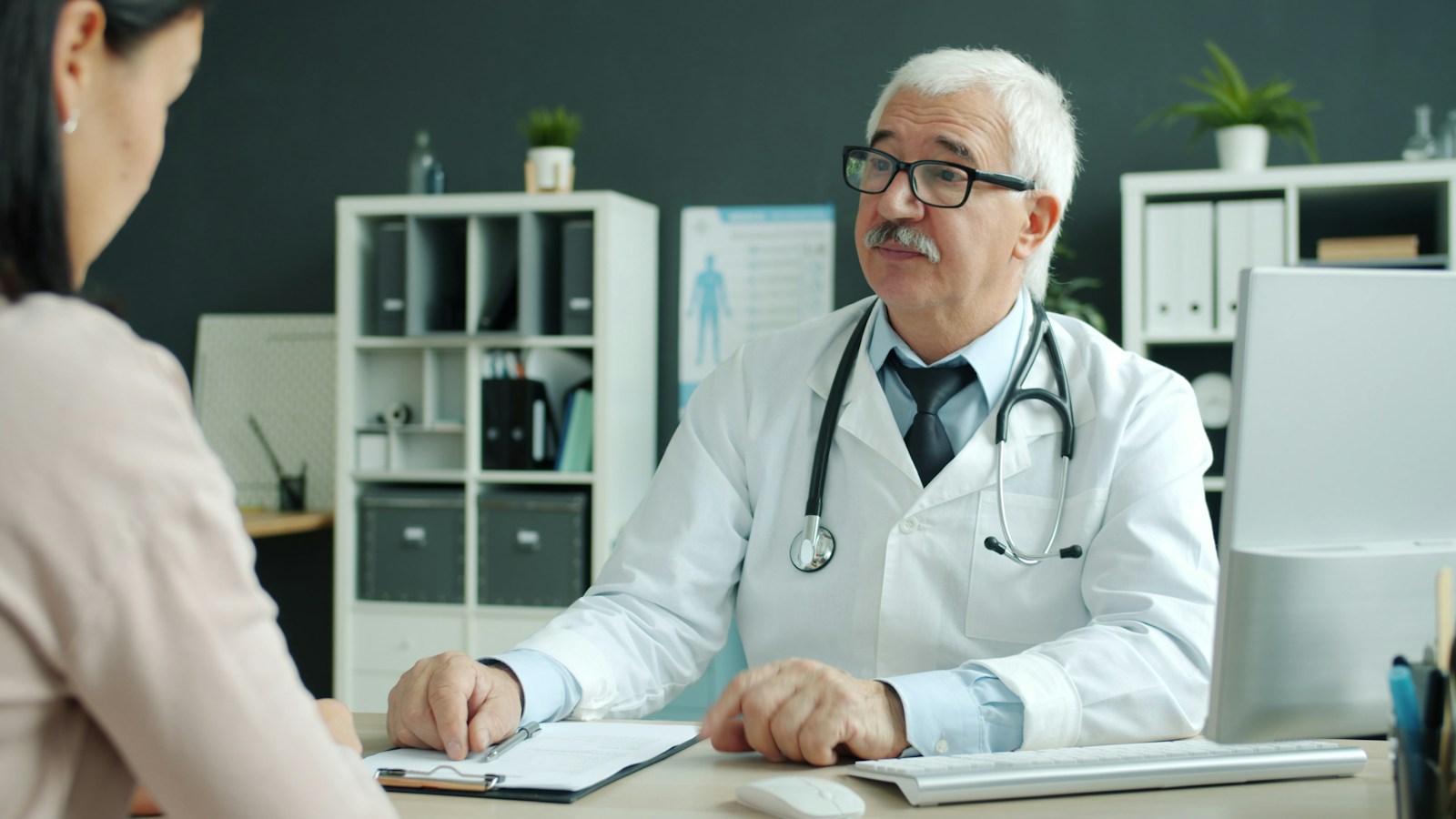 A physician in a white coat consulting with a patient during an office visit